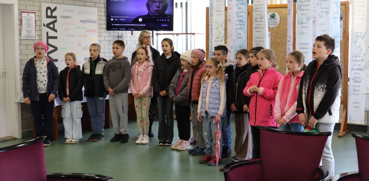 A Tiszaújvárosi Hunyadi Mátyás Általános Iskola diáájkai verset mondanak a könyvtár Folyóiratolvasójában.